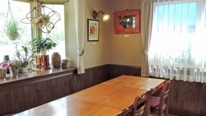 A dining area with a wooden table and chairs, a window with curtains, and various potted plants on the windowsill.