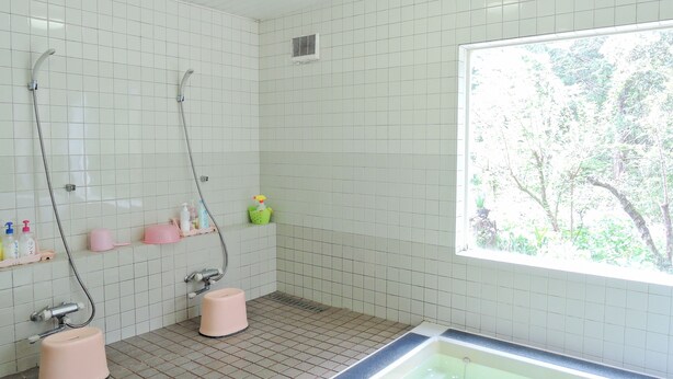A bathroom with white tiled walls, a shower, a bathtub, and a window with a view of trees.