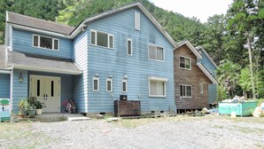 A two-story house with a front porch, a small garden, and a gravel driveway.
