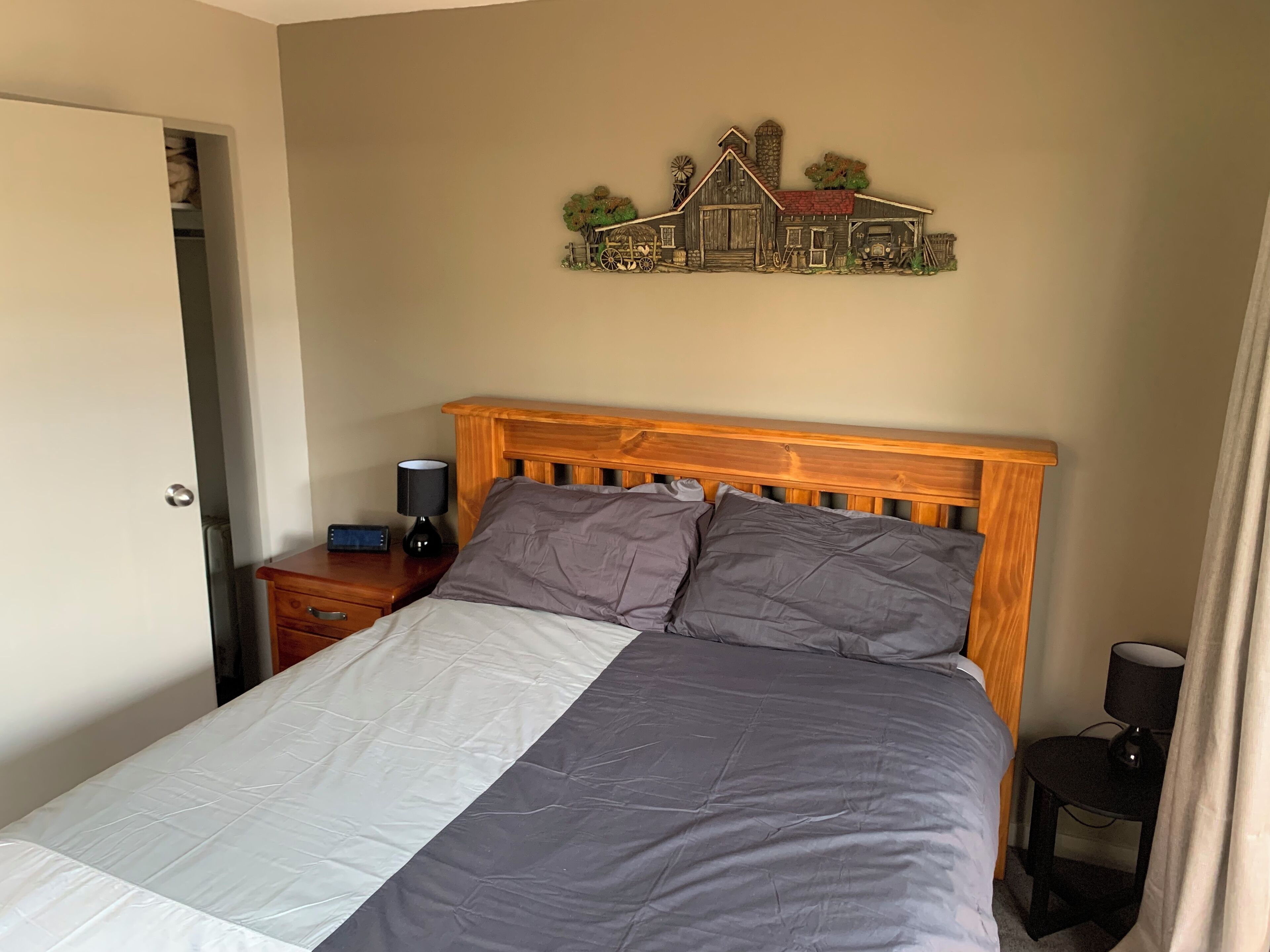 Une chambre à coucher avec un lit en bois, une table de chevet avec une lampe, un élément décoratif fixé au mur et une porte.