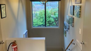 Eine Treppe mit einem Feuerlöscher, ein Fenster mit Blick auf Grünflächen und Bilder an der Wand.