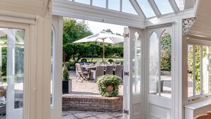 Una conserjería abierta con techo de vidrio, una zona de patio con mobiliario exterior y vistas a un jardín.