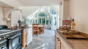 Una cocina con piso de baldosas de piedra, gabinetes de madera, una estufa de acero inoxidable y un comedor con mesa y sillas.