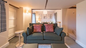 Una sala de estar acogedora con un sofá verde, dos cojines rojos, una mesita redonda y una lámpara.
