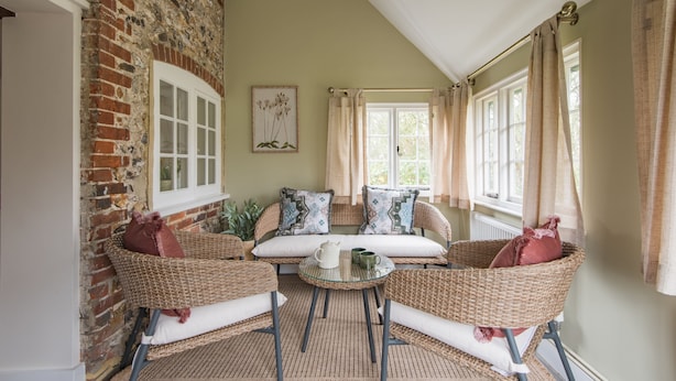 Una habitación acogedora con muebles de mimbre, una pared de ladrillo y una ventana con cortinas.
