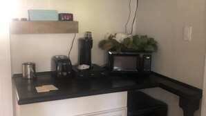 A kitchen with a black countertop, a microwave, a toaster, a coffee maker, and a clock. - The Russell Lake House (Winter Haven)