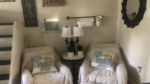 A cozy room with two armchairs, each with a cushion featuring a fish design. There is a small table with two lamps and a couple of potted plants. A decorative sign on the wall reads "hello." - The Russell Lake House (Winter Haven)