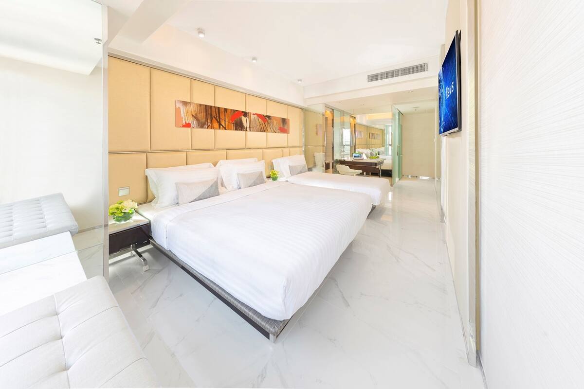 Una habitación de hotel moderna con una cama grande, una zona de estar y un baño con espejo.