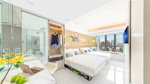 A modern hotel room with a large bed, a desk with a laptop, a mirror, and a city view.