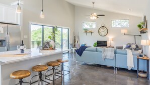 Una cocina moderna con barra, una sala de estar con sofá y televisor, y un comedor con mesa y sillas.