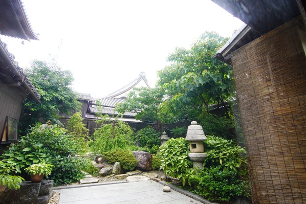 A traditional Japanese garden with stone lanterns, a koi pond, and a wooden building with a tiled roof. - Honmachi Juku (Hikone)