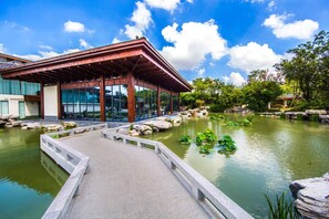 Un pavillon traditionnel en bois, doté d’une structure vitrée, d’un chemin de pierre et d’un bassin orné de nénuphars.