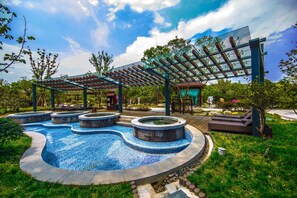 A swimming pool with a curved design, surrounded by a wooden deck and covered areas. - Slender West Lake Hot Spring Resort (Yangzhou)