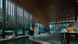 Un espace spa moderne doté d’une grande piscine intérieure, de lambris en bois au plafond et offrant une vue sur un paysage naturel grâce à de grandes fenêtres.