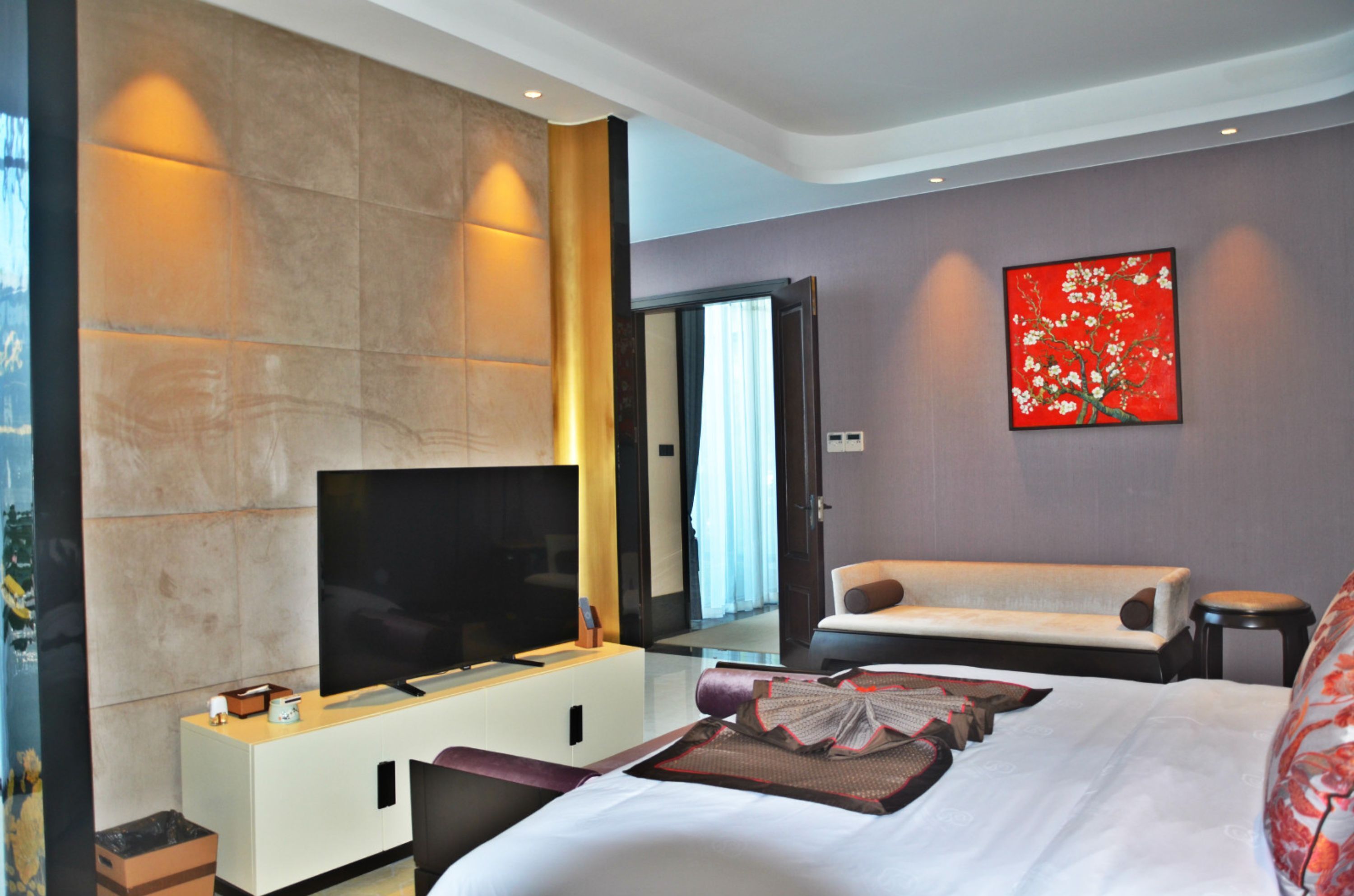 Una habitación de hotel moderna con una cama grande, un televisor de pantalla plana, un sofá y una obra de arte roja en la pared.