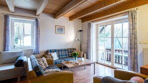 Een gezellige woonkamer met een bank, fauteuils en een salontafel. Er zijn grote ramen en uitzicht op het omliggende landschap.