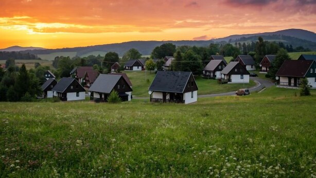 Een landelijk dorp met traditionele huizen, een kronkelende weg en een zonsondergang op de achtergrond.