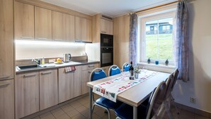 Een compacte keuken met houten kastjes, een spoelbak en een eethoek met een tafel voor vier personen.