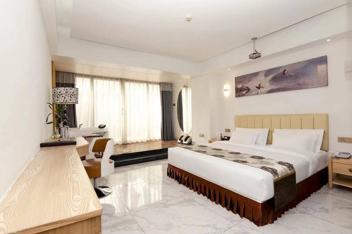 A modern hotel room with a large bed, a desk, a chair, and a painting on the wall.
