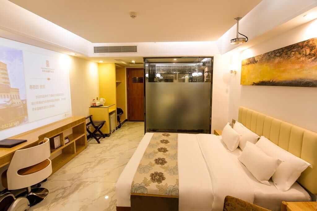 A hotel room with a bed, a desk, a chair, a small kitchenette, and a large painting on the wall.