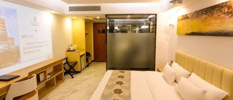 A hotel room with a bed, a desk, a chair, a small kitchenette, and a large painting on the wall.
