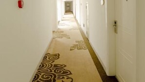 Pasillo de hotel con alfombra estampada, paredes blancas y puertas a ambos lados.