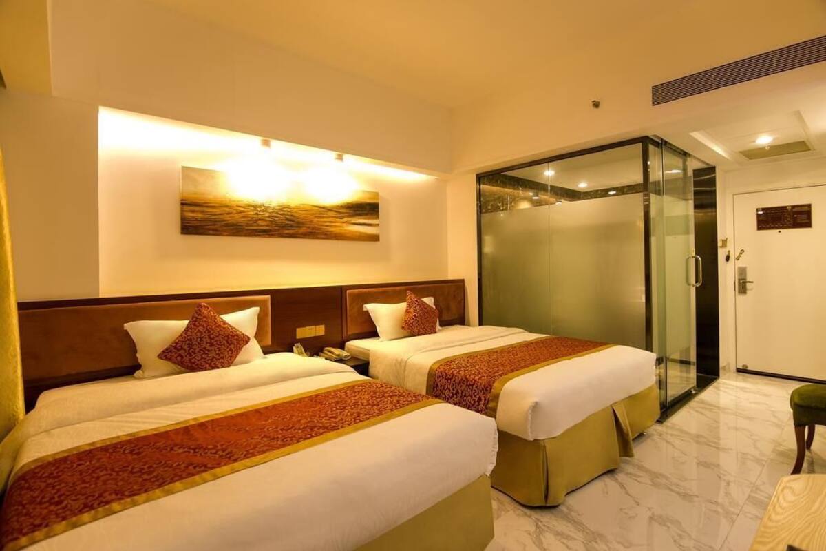 A hotel room with two beds, a glass-enclosed shower, a painting on the wall, and a marble floor.