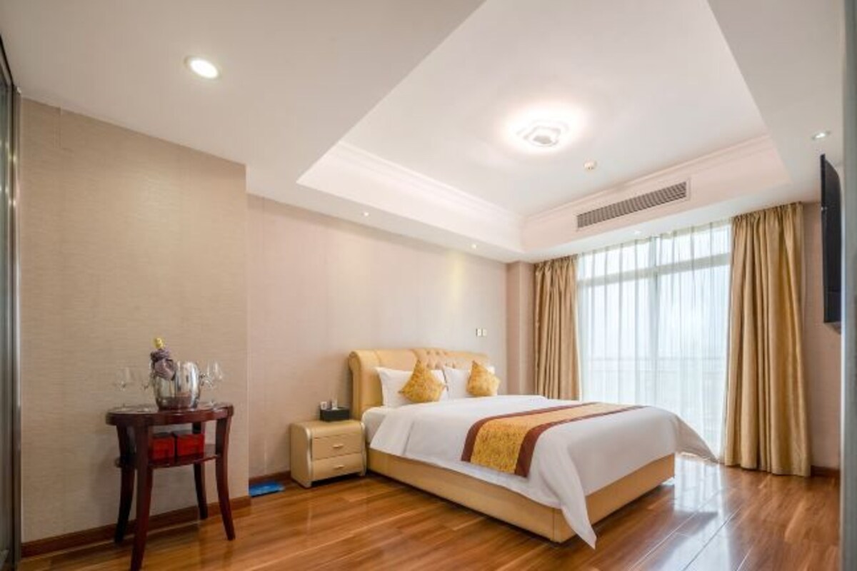 Una habitación de hotel con una cama grande, mesitas de noche, una pequeña mesa con un florero y un televisor en la pared.