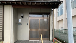 Entrada de un edificio con una reja metálica, un banco de madera y un camino de baldosas.