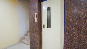 A hallway with a marble wall, a door with a keypad, and a small window. - OYO 63371 R Square Stay (Hyderabad)