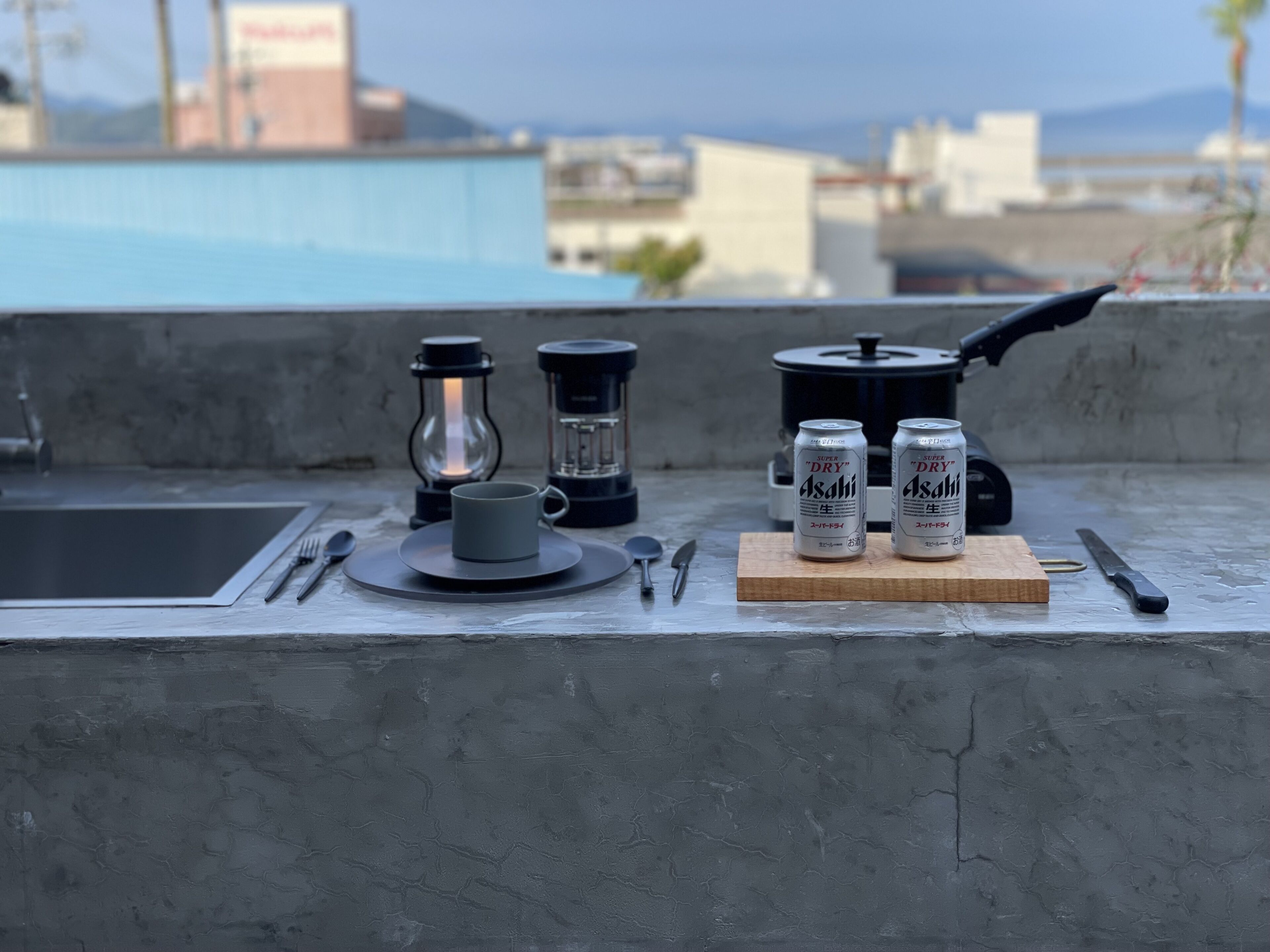Un espace de restauration aménagé sur un toit, comprenant une machine à café, deux canettes de bière Asahi, une tasse et une planche à découper en bois.