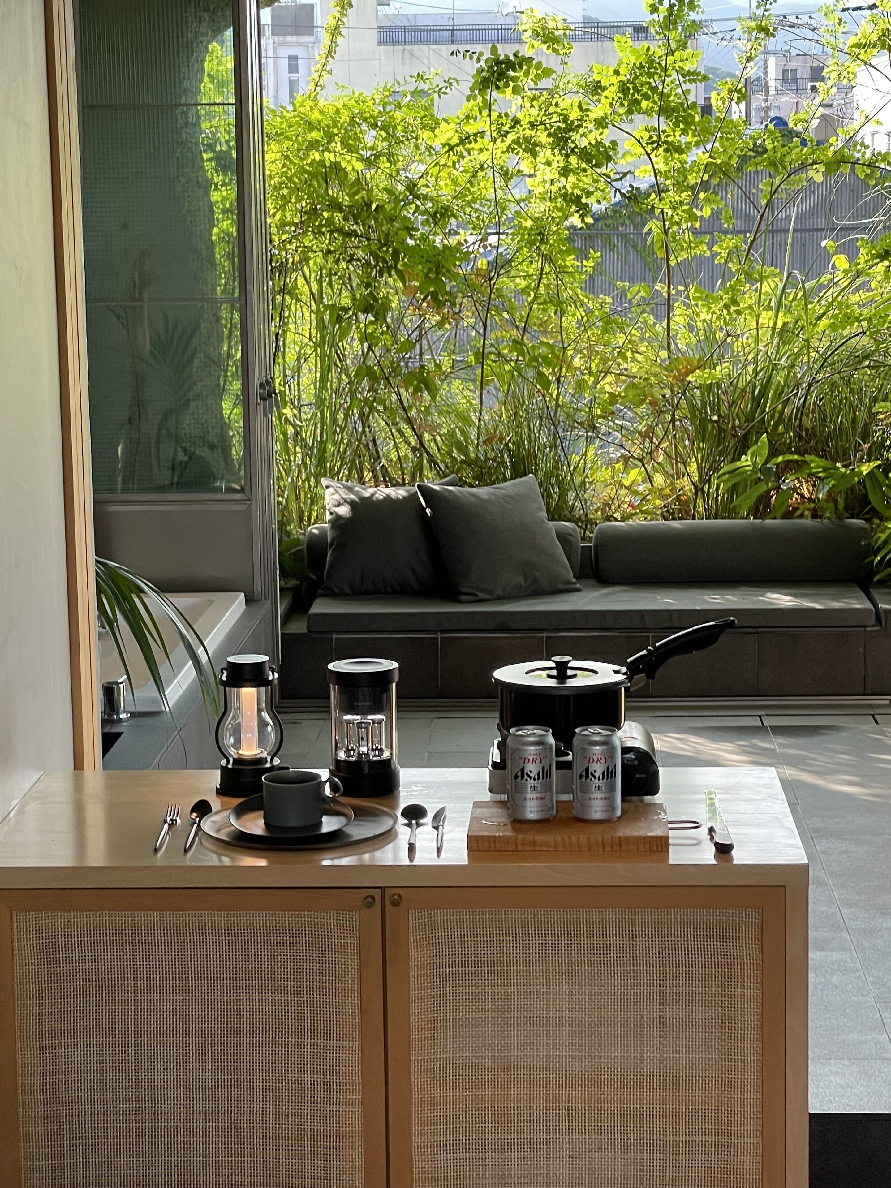 A modern living room with a sofa, a dining table with a coffee maker, and a view of greenery and buildings.