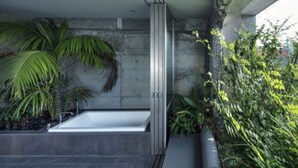 Ein modernes Badezimmer mit einer freistehenden Badewanne, einer Betonwand und Topfpflanzen.
