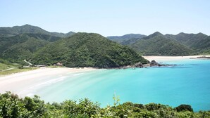 Eine Küstenlandschaft mit Strand, klarem türkisblauem Wasser und üppigen grünen Hügeln.