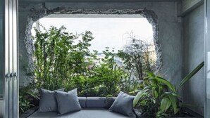 Ein moderner Außenbereich mit integrierter Sitzbank und Kissen, umgeben von üppigem Grün und Blick auf die Stadtlandschaft.