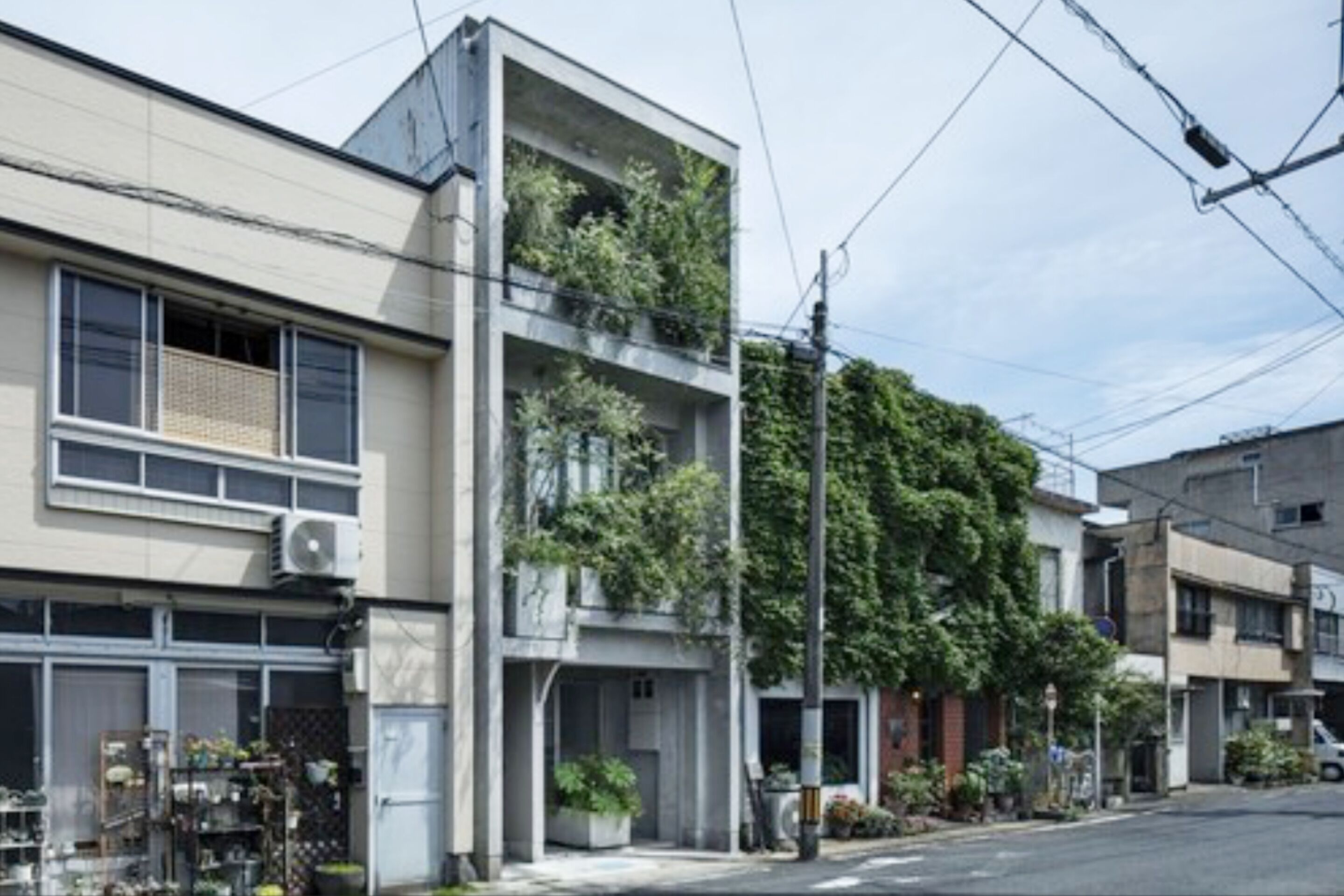 Un edificio moderno de dos pisos con un balcón en el nivel superior, rodeado de otras edificaciones residenciales.