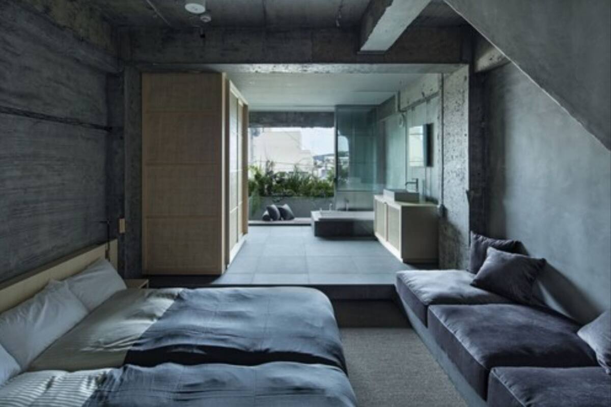 A modern bedroom with a large bed, a sofa, and a view of the city through an open door.