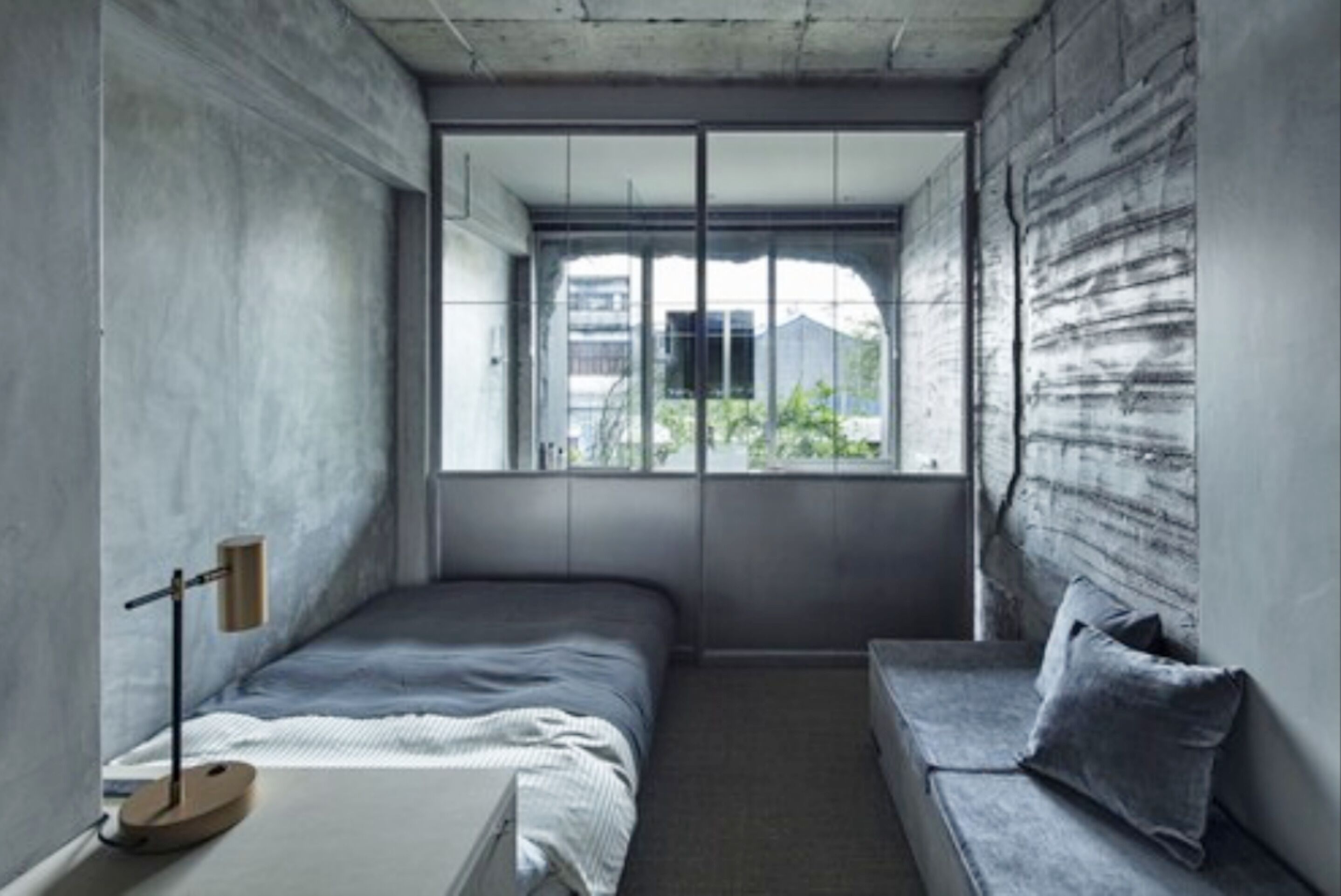 Une chambre à coucher moderne avec un lit, un banc et une fenêtre donnant sur des bâtiments et de la verdure.