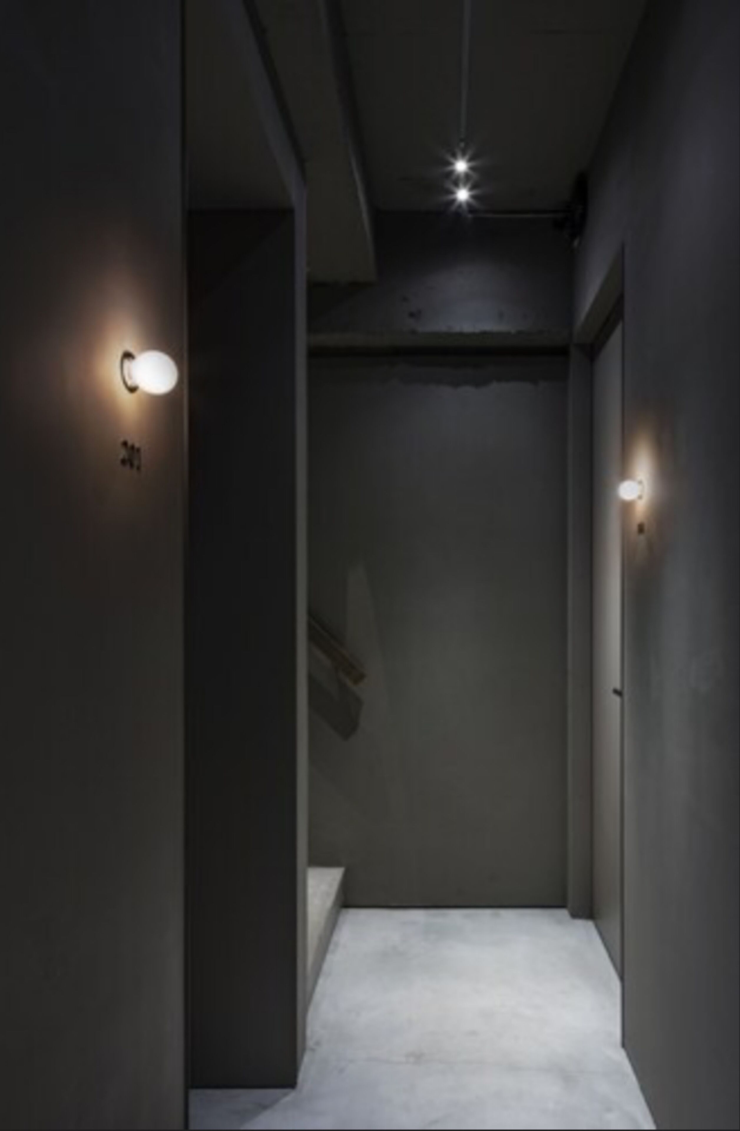 A narrow, dimly lit hallway with two wall-mounted light fixtures and a visible door at the end.