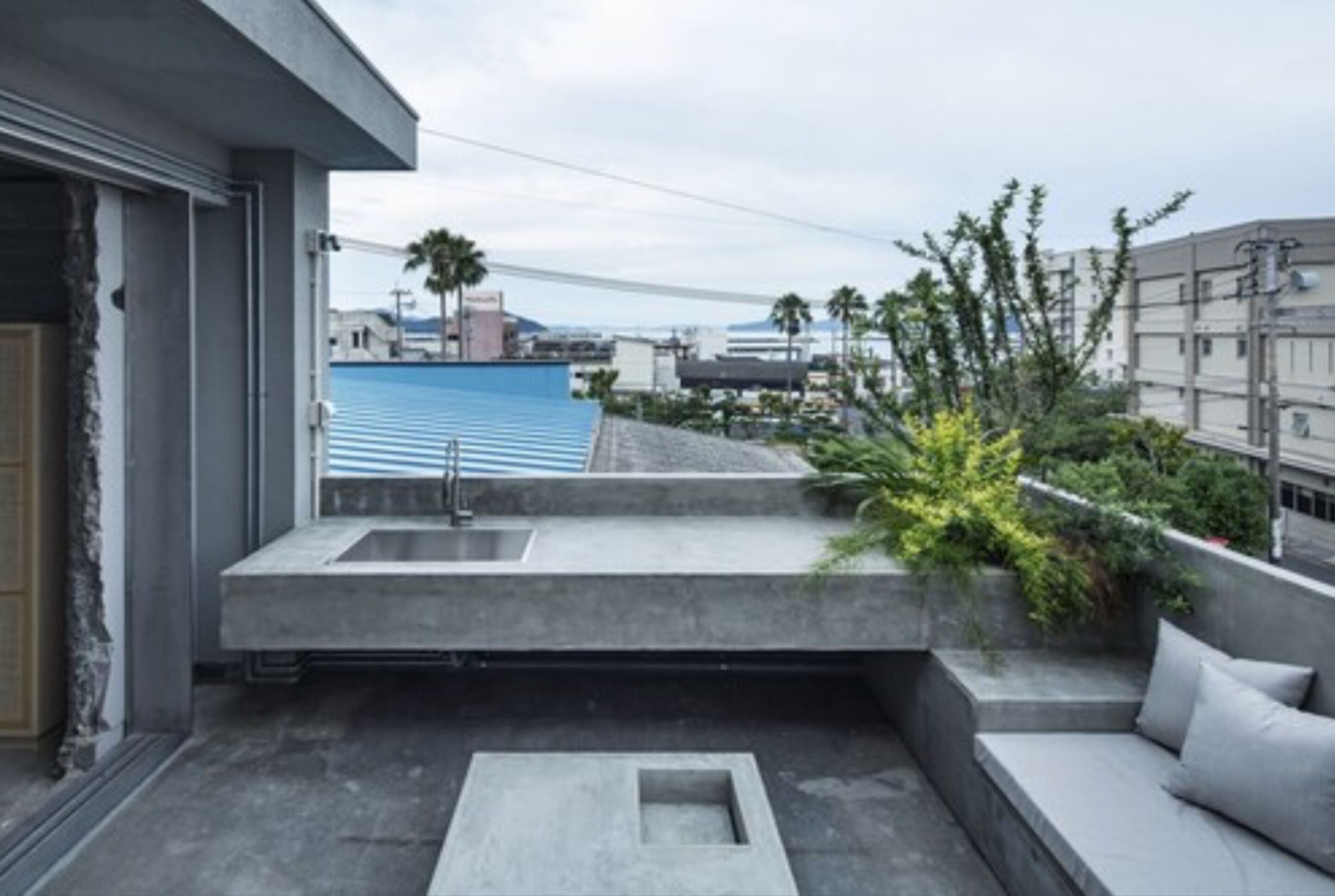 A modern balcony with a concrete sink, seating area, and a view of a bridge and buildings.