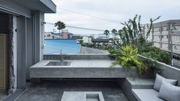 A modern balcony with a concrete sink, seating area, and a view of a bridge and buildings.