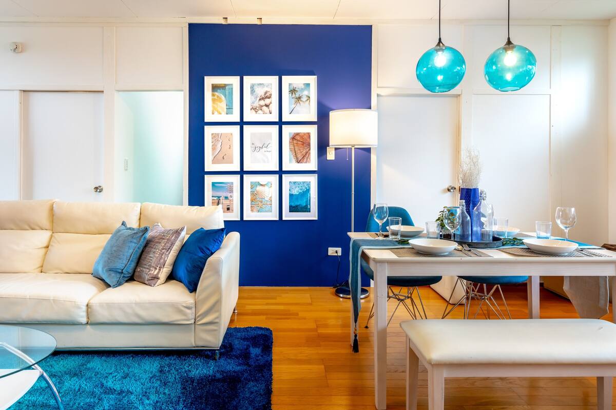 Een moderne woonkamer met een blauwe accentmuur, een witte bank, een eettafel gedekt voor twee personen en een blauw vloerkleed.