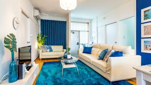 Una sala de estar moderna con alfombra azul, un sofá blanco, un sofá beige y una mesa de centro de vidrio.
