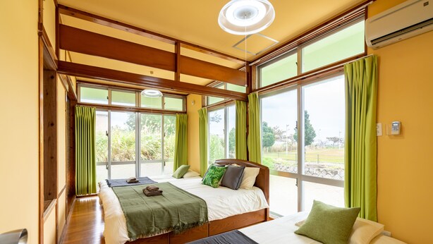 Una habitación con dos camas, ventanas amplias y un ventilador de techo.