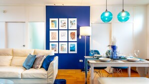 Una sala de estar moderna con una pared azul de acento, un sofá blanco, una mesa de comedor para dos personas y una alfombra azul.