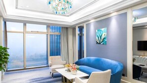 A modern hotel room with a large window, a blue sofa, a dining table, and a chandelier. - Lily's Hotel Hangzhou (Hangzhou)