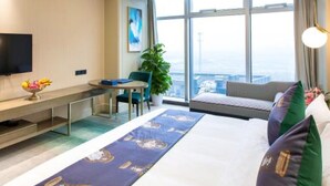 A hotel room with a bed, a desk, a chair, a TV, and a large window offering a city view. - Lily's Hotel Hangzhou (Hangzhou)