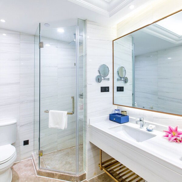 A modern bathroom with a glass shower enclosure, a white sink with a blue soap dish, and a large mirror.