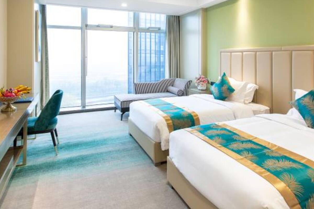 A hotel room with two beds, a desk, and a large window.