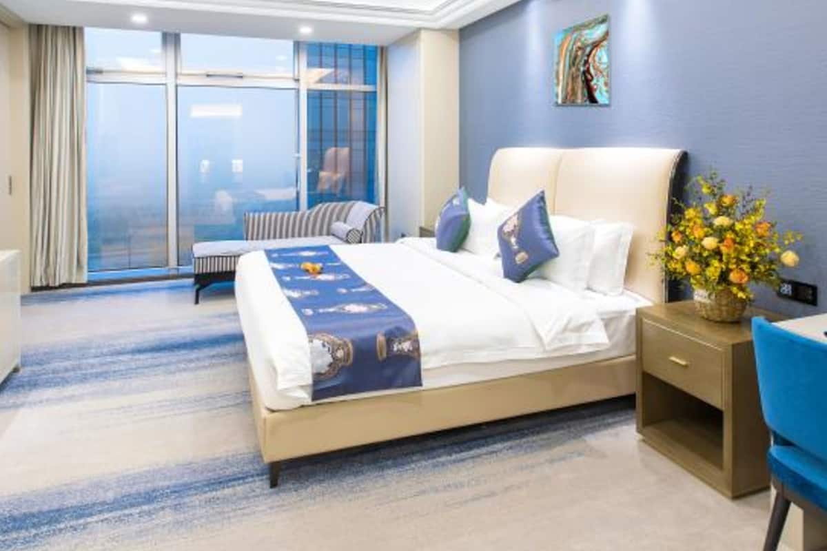 A hotel room with a large bed, a desk, a chair, a window with curtains, and a painting on the wall.